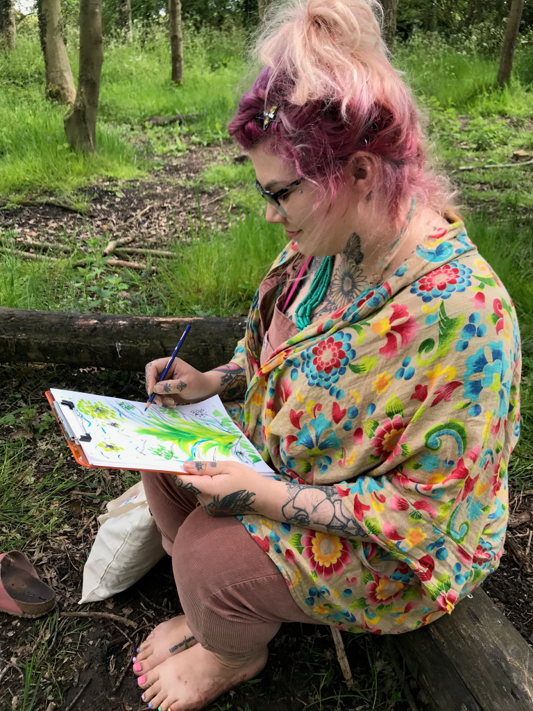 woman wearing colourful clothes sitting peacefully in the woodland drawing and painting nature